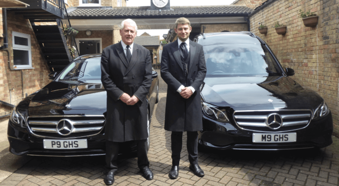 Funeral directors stood in front of funeral cars